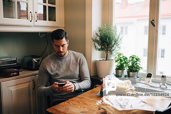 Man using mobile phone while sitting at table in kitchen