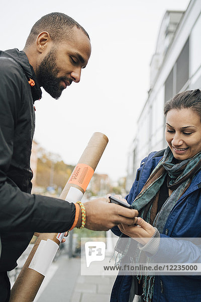 Lächelnde Frau unterschreibt am Handy für ihre Paketzustellung von männlichen Arbeitern