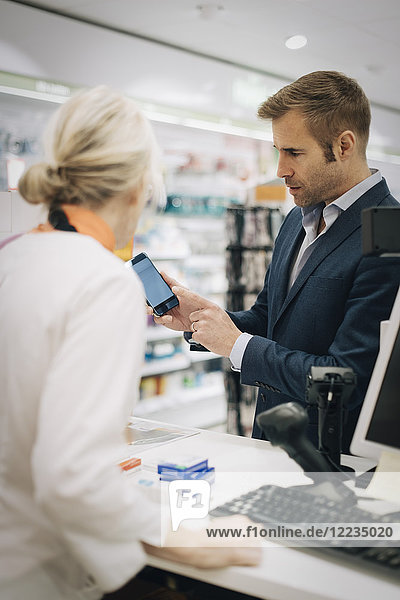 Reifer Mann zeigt Smartphone der Besitzerin an der Kasse in der Apotheke