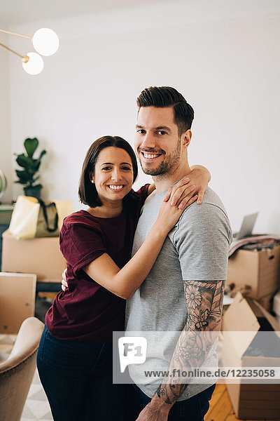 Porträt eines lächelnden Paares  das sich während des Umzugs im Wohnzimmer umarmt.