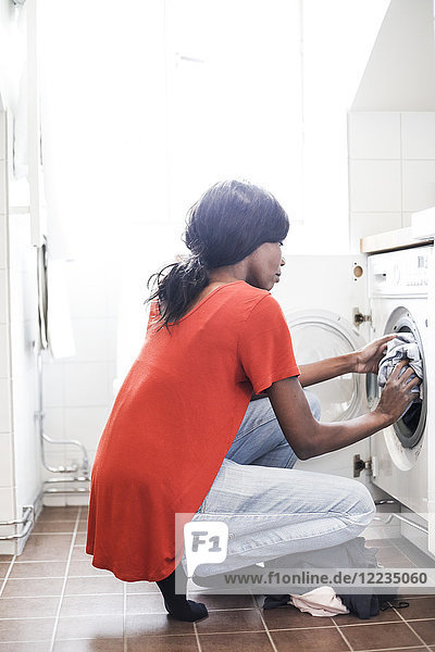 Durchgehende Seitenansicht der mittleren erwachsenen Frau beim Wäschewaschen zu Hause