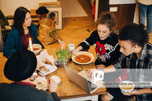 Blickwinkel auf Geschäftsleute die über den Laptop diskutieren während sie am Tisch im Kreativbüro zu Mittag essen.