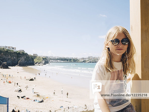 Blondes Mädchen sitzt an einer Holzsäule am Strand gegen den Himmel an einem sonnigen Tag.