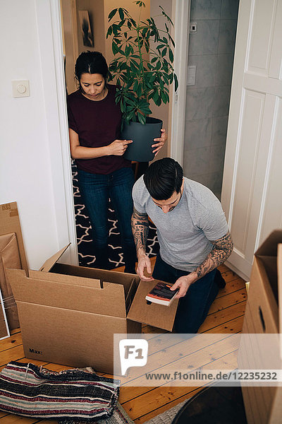 Woman holding potted plant while man reading book during unpacking boxes at house