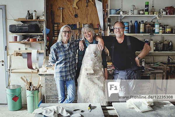 Porträt von fröhlichen Senior-Mitarbeitern  die in der Werkstatt gegen Werkzeuge stehen
