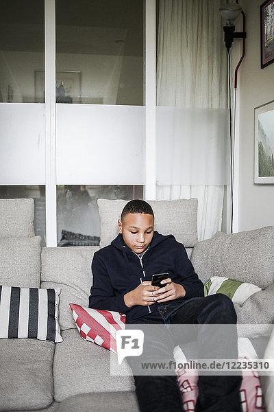 Teenage boy using smart phone on sofa at home