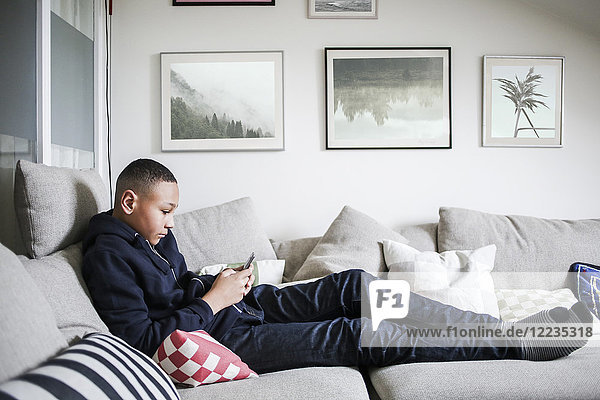 Full length side view of teenage boy using mobile phone on sofa at home