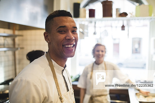 Porträt eines lächelnden jungen Kochs in der Restaurantküche mit Kollegen