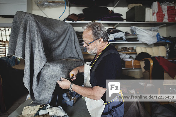 Senior männlicher Besitzer schneidet grauen Stoff  während er in der Werkstatt steht.