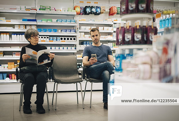 Customers sitting on chairs against medicine rack at pharmacy store