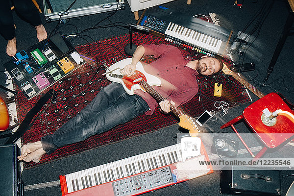 Hochwinkelansicht eines Mannes der Gitarre spielt während er im Studio auf dem Teppich liegt.