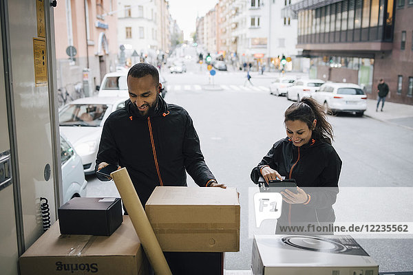 Smiling coworkers using technologies while examining packages in delivery van