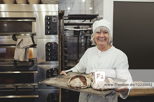 Lächelnder Bäcker mit frisch gebackenem Brot in der Backstube