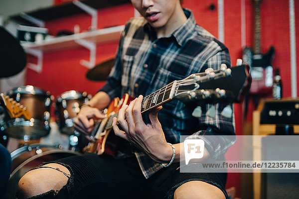 Mittelteil des Mannes der Gitarre spielt während er im Aufnahmestudio sitzt.