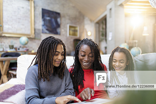 Smiling mother and daughters looking at photo album on sofa
