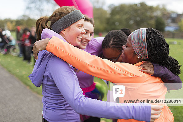 Happy female runners hugging at charity run finish line  celebrating