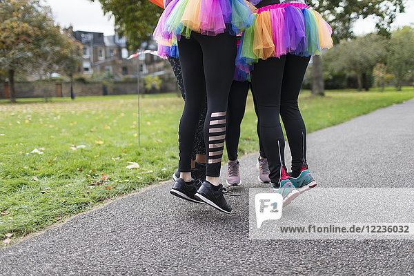 Enthusiastic female runners in tutus jumping on park path