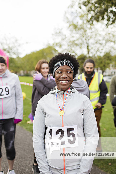 Portrait lächelnde  selbstbewusste Läuferin mit Medaille beim Charity-Lauf im Park