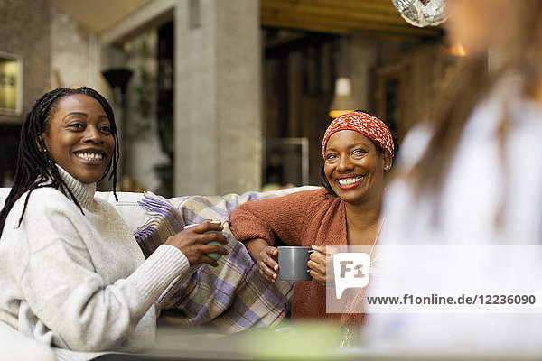 Smiling women talking and drinking coffee on sofa
