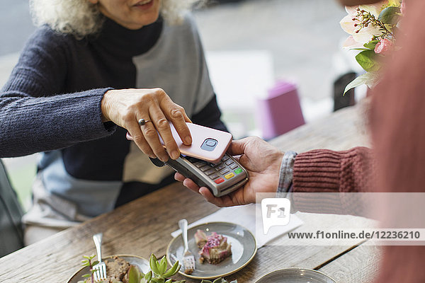 Frau mit Smartphone mit kontaktloser Bezahlung im Cafe