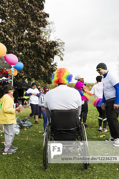 Man in wheelchair wearing clown wig at charity race in park