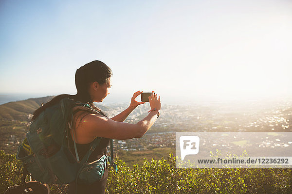 Backpackerin mit Fotohandy fotografiert sonnige Stadtansicht