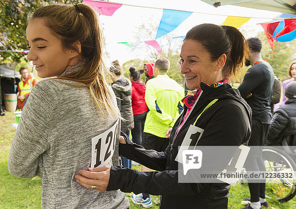 Mother pinning marathon bib on daughter at charity run in park