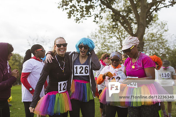 Portrait playful female runners in wigs and tutus at charity run in park