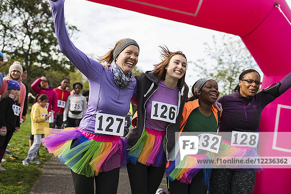 Enthusiastic female runners in tutus cheering  crossing finish line at charity run  celebrating