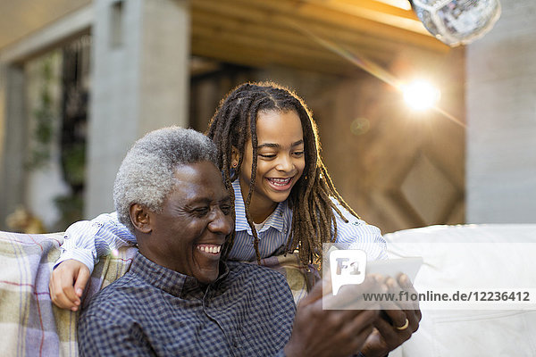 Grandfather and granddaughter using smart phone on sofa