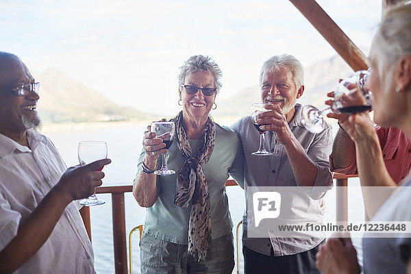 Happy active senior friends drinking wine on balcony