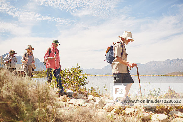 Active senior friends hiking along sunny summer lake