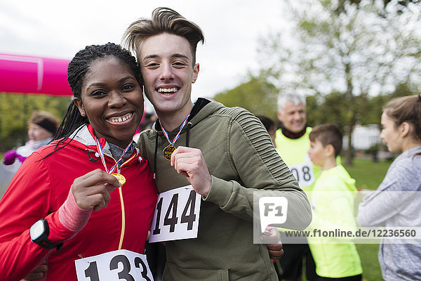 Portrait smiling  confident couple runners showing medals at charity run in park