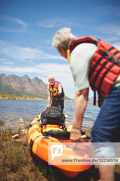 Active senior couple preparing kayak at sunny  summer lake