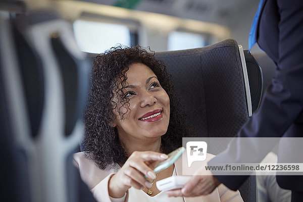 Smiling woman with smart phone using contactless payment on passenger train