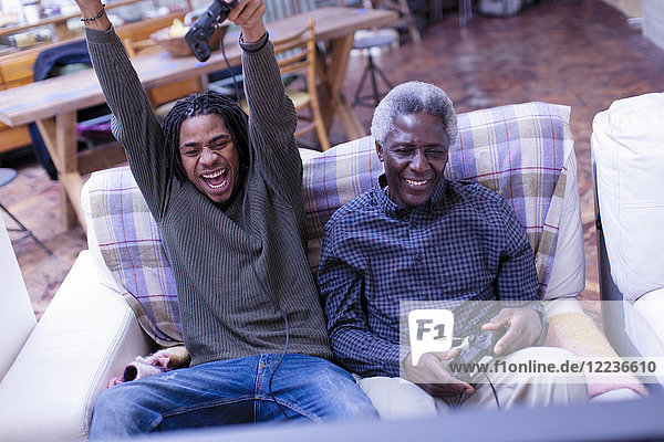 Enthusiastic grandfather and grandson playing video game on sofa