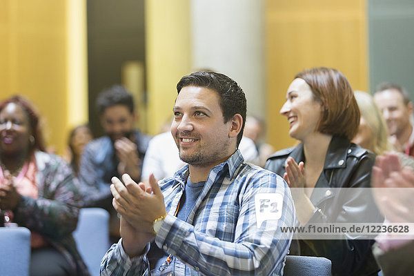 Smiling man clapping in conference audience