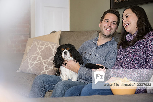 Happy mid adult couple relaxing on sofa with dog