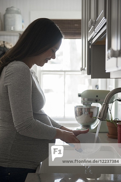 Schwangere Frau wäscht Schüssel in Küchenspüle