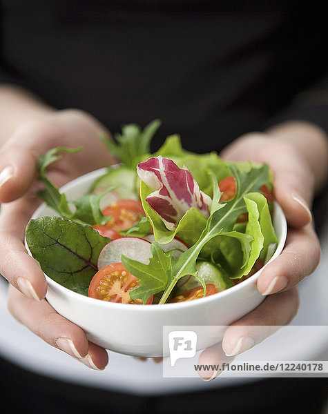 Hands holding a small white ball with mixed salad