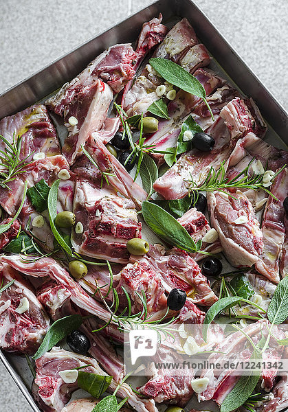 Rohe Lammfleischstücke mit Knoblauch  Oliven  Salbei  Rosmarin und Lorbeerblättern auf einem Backblech