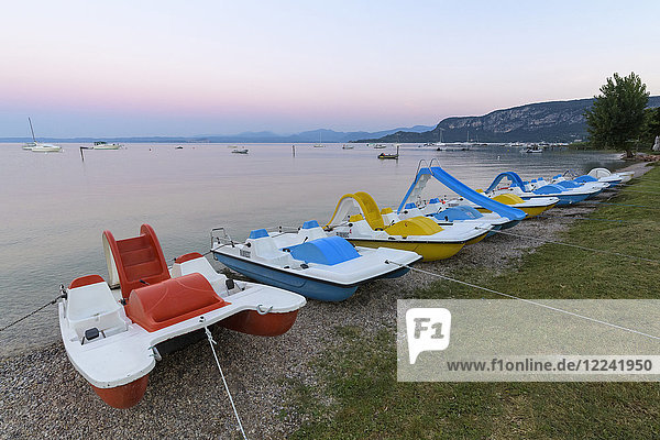 Reihe bunter Tretboote am Strand in der Morgendämmerung am Gardasee (Lago di Garda) bei Bardolino in Venetien  Italien