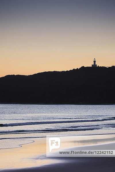 Silhouette of Cape Byron Lighthouse on hilltop and beach at sunset at Byron Bay in New South Wales  Australia