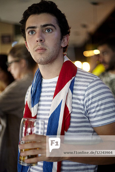 British football fan watching match in bar with flag draped around neck
