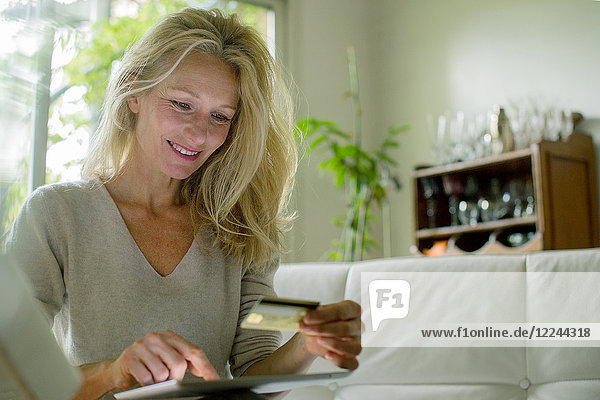 Reife Frau mit digitalem Tisch zum Online-Shopping