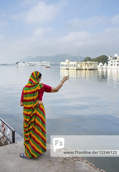 Im sanften Morgenlicht blickt eine Rajasthani-Frau in einem Sari über den Pichola-See  mit dem berühmten Lake Palace im Hintergrund  Udaipur  Rajasthan  Indien  Asien