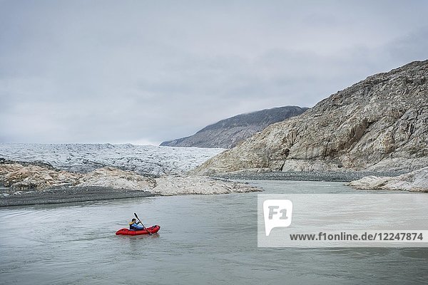 Man with Packraft on river  behind glacier and rocks  cloudy  Greenland  North America