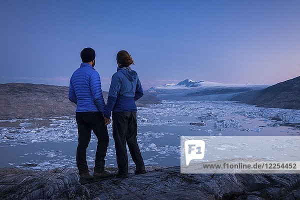 Couple stands on rocks and looks at glacial lake with small icebergs  evening mood  Greenland  North America