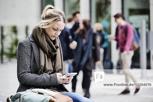 Young woman  student  sitting on campus with her smartphone  Cologne  North Rhine-Westphalia  Germany  Europe
