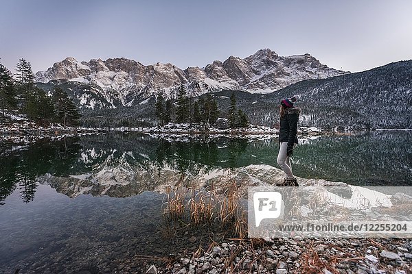 Young woman standing on the shore  Eibsee lake in winter with Zugspitze  Spiegelung  Wetterstein range  Upper Bavaria  Bavaria  Germany  Europe